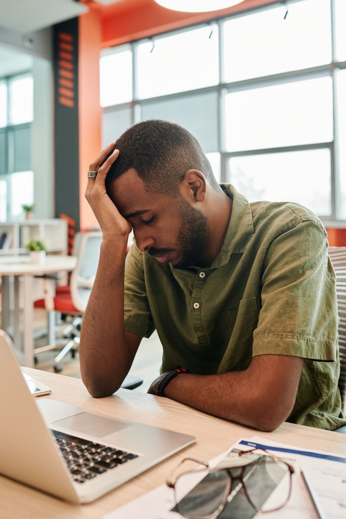 African American man experiencing burnout at office desk with a laptop.
